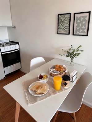 A modern kitchen with a stove, oven, and dining table set with breakfast items. - Frente a River. Balcón sobre Av. Libertador, con vista al Monumental. (Buenos Aires)