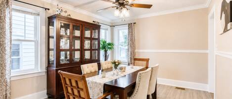 Une salle à manger avec une table en bois, des chaises, un ventilateur de plafond et un buffet aux portes vitrées.