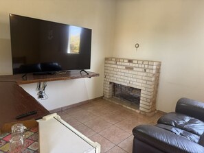 Una sala de estar con un televisor de pantalla plana montado en un estante de madera, una chimenea de ladrillo y un sofá de cuero.