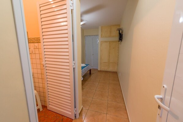 A narrow hallway with a closed door, a small stool, and a bed with a blue cover.