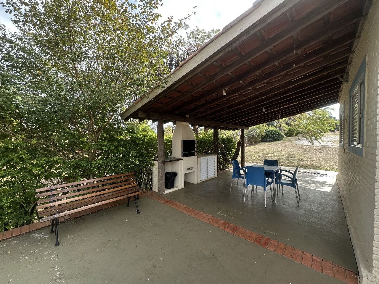An outdoor patio with a barbecue grill, a wooden bench, and blue chairs.