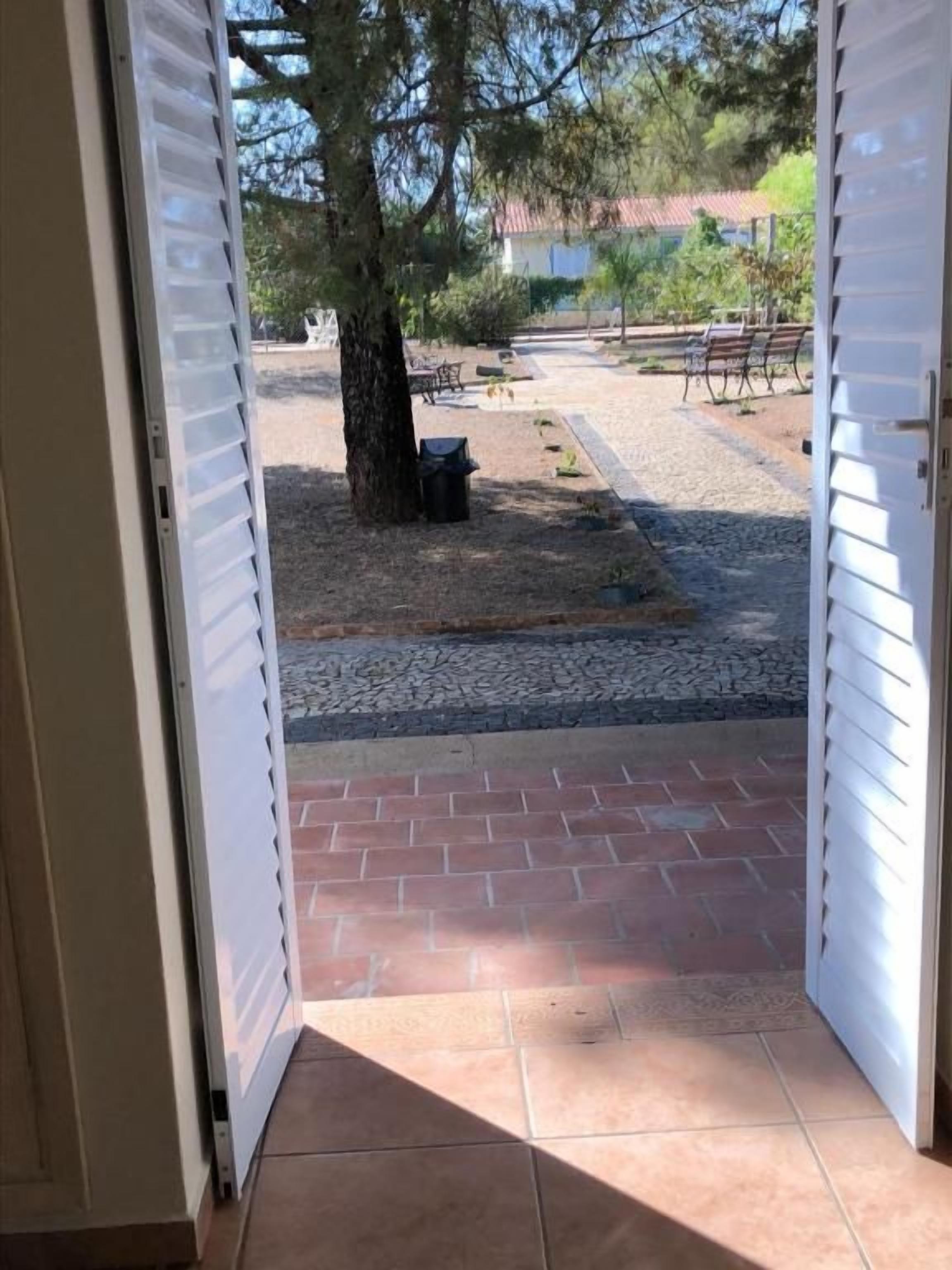 An open door leading to a patio area with a gravel path, a tree, and outdoor furniture.