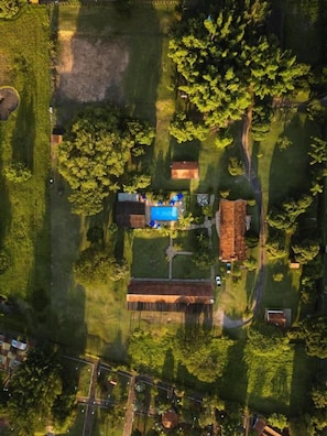 An aerial view of a property with a swimming pool, a large tree, and a building with a sloped roof.