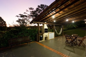 An outdoor patio area with a wooden pergola, a hammock, a bench, and a table with chairs.