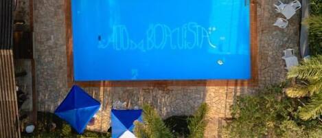 A swimming pool with a blue sign, surrounded by greenery and outdoor furniture.