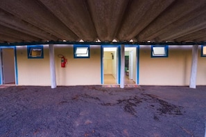 A covered outdoor area with a dirt floor, multiple doorways leading to rooms, and a fire extinguisher mounted on the wall.