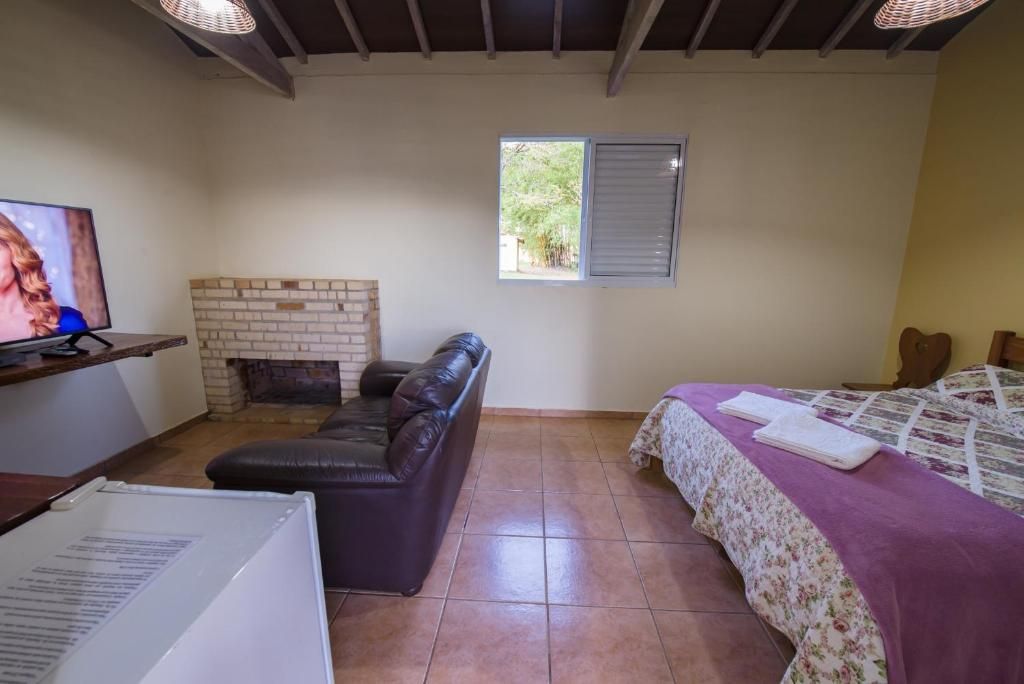 A room with a fireplace, a leather sofa, a bed with a floral bedspread, and a television on a stand.