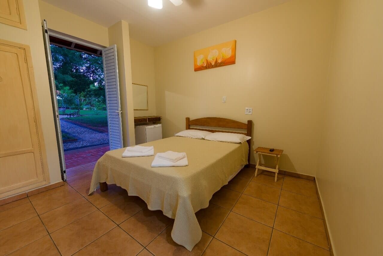 A bedroom with a bed, a nightstand, a painting, and a door leading to an outdoor area.