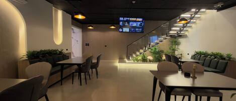 Un interior moderno con una escalera, zonas de estar y una pantalla de proyección mostrando contenido.