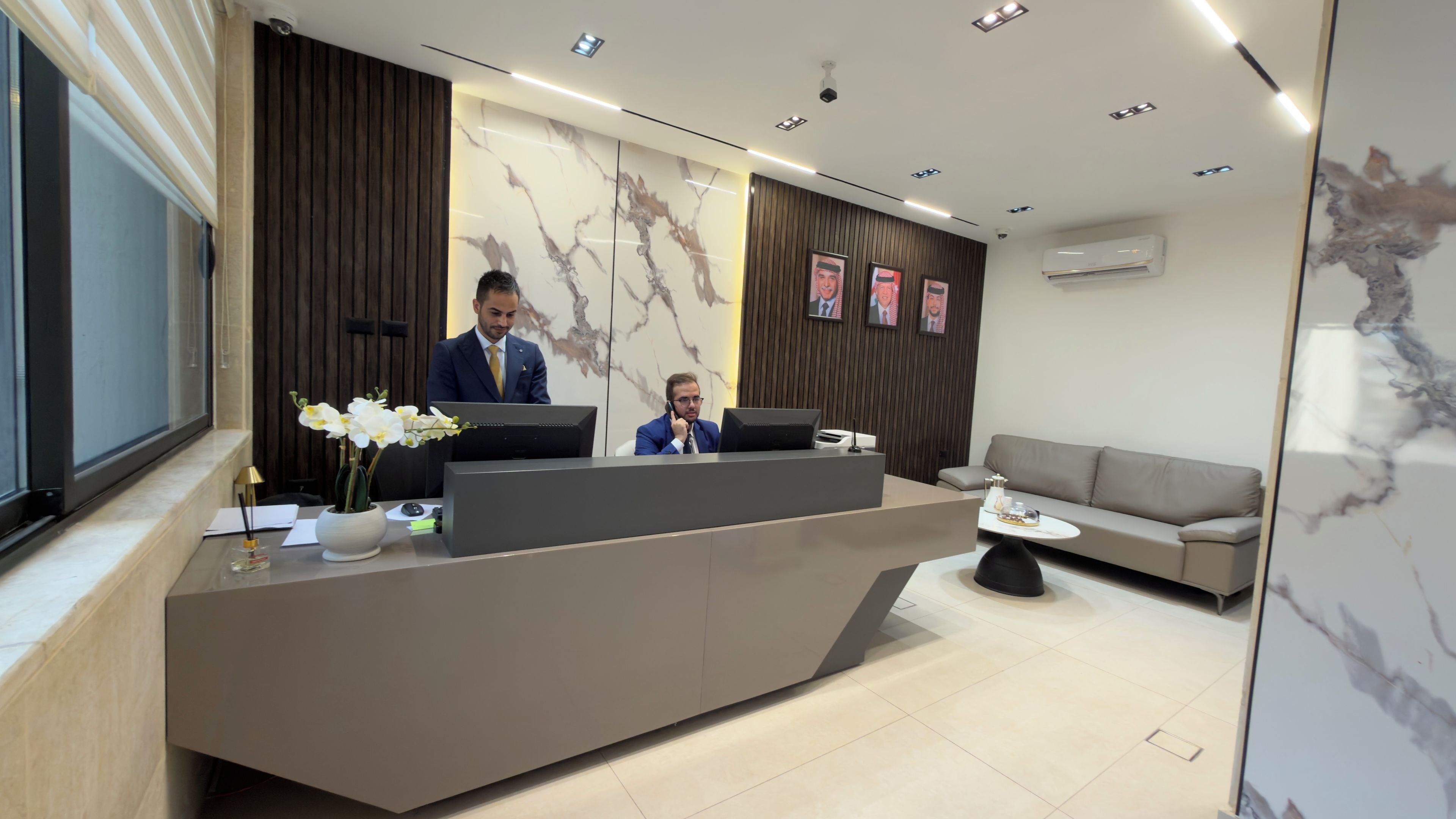 A reception desk with two staff members, a sofa, and a wall-mounted air conditioner.
