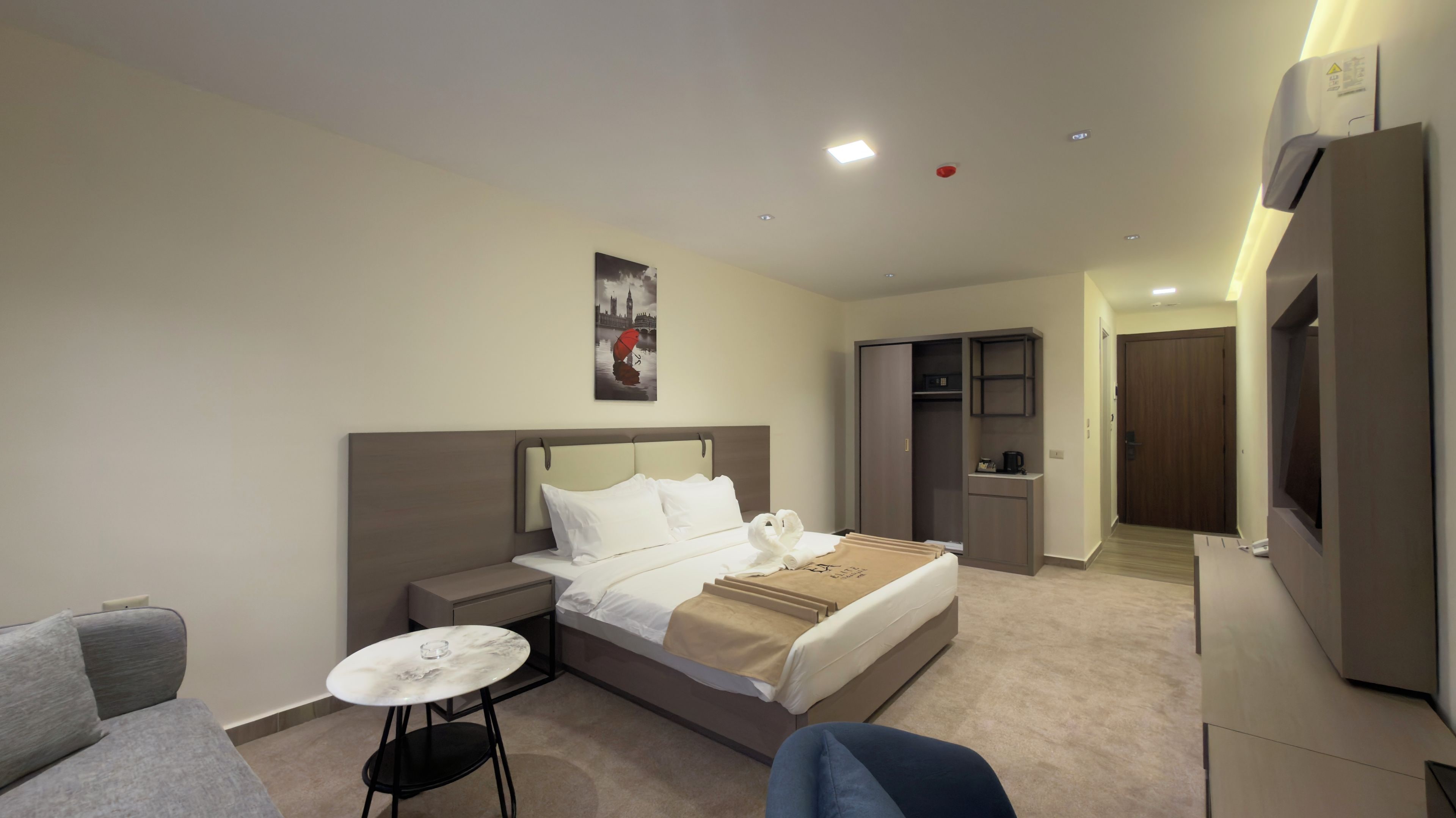 A hotel room with a bed, a small table, a chair, a wardrobe, and a mirror.