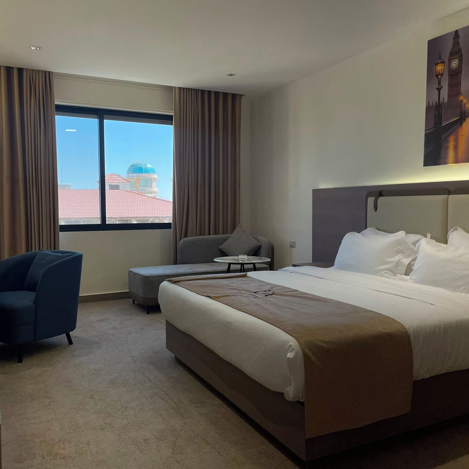 A hotel room with a large bed, a desk, a chair, and a view of a building with a dome through a window.