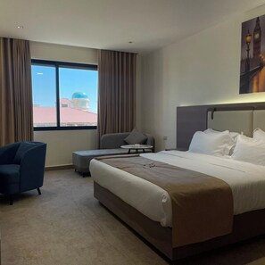 Ein Hotelzimmer mit einem großen Bett, einem Schreibtisch, einem Stuhl und Blick auf ein Gebäude mit einer Kuppel durch ein Fenster.