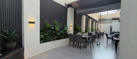 Een moderne buiten eethoek met meerdere tafels en stoelen, omringd door verticale tuinen en wandlampen.