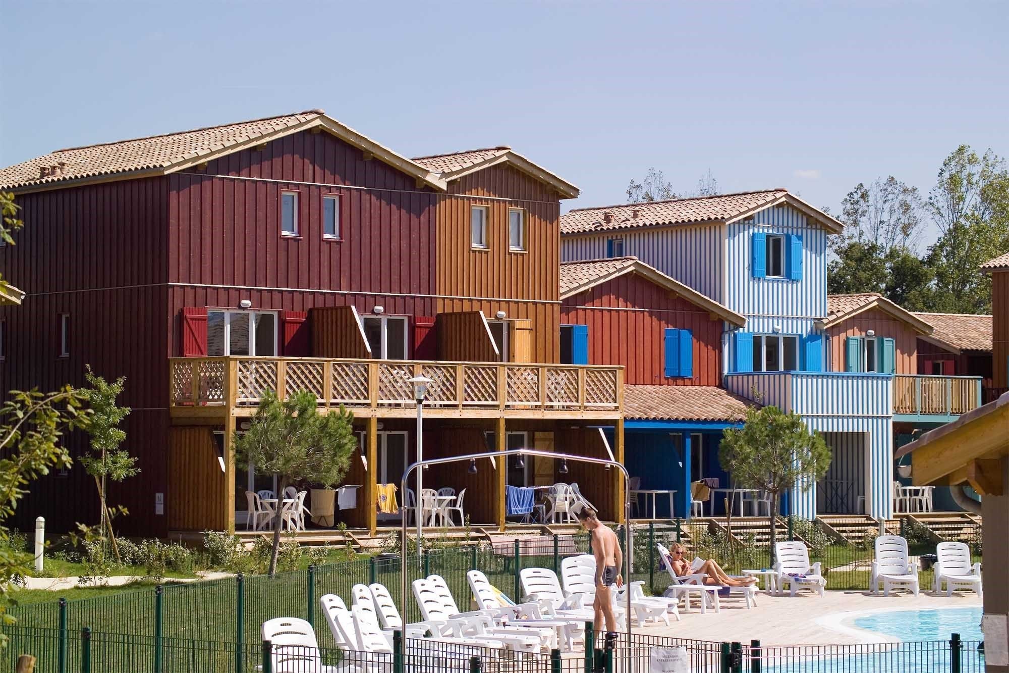 Un hotel con edificios de colores, piscina y mobiliario exterior.