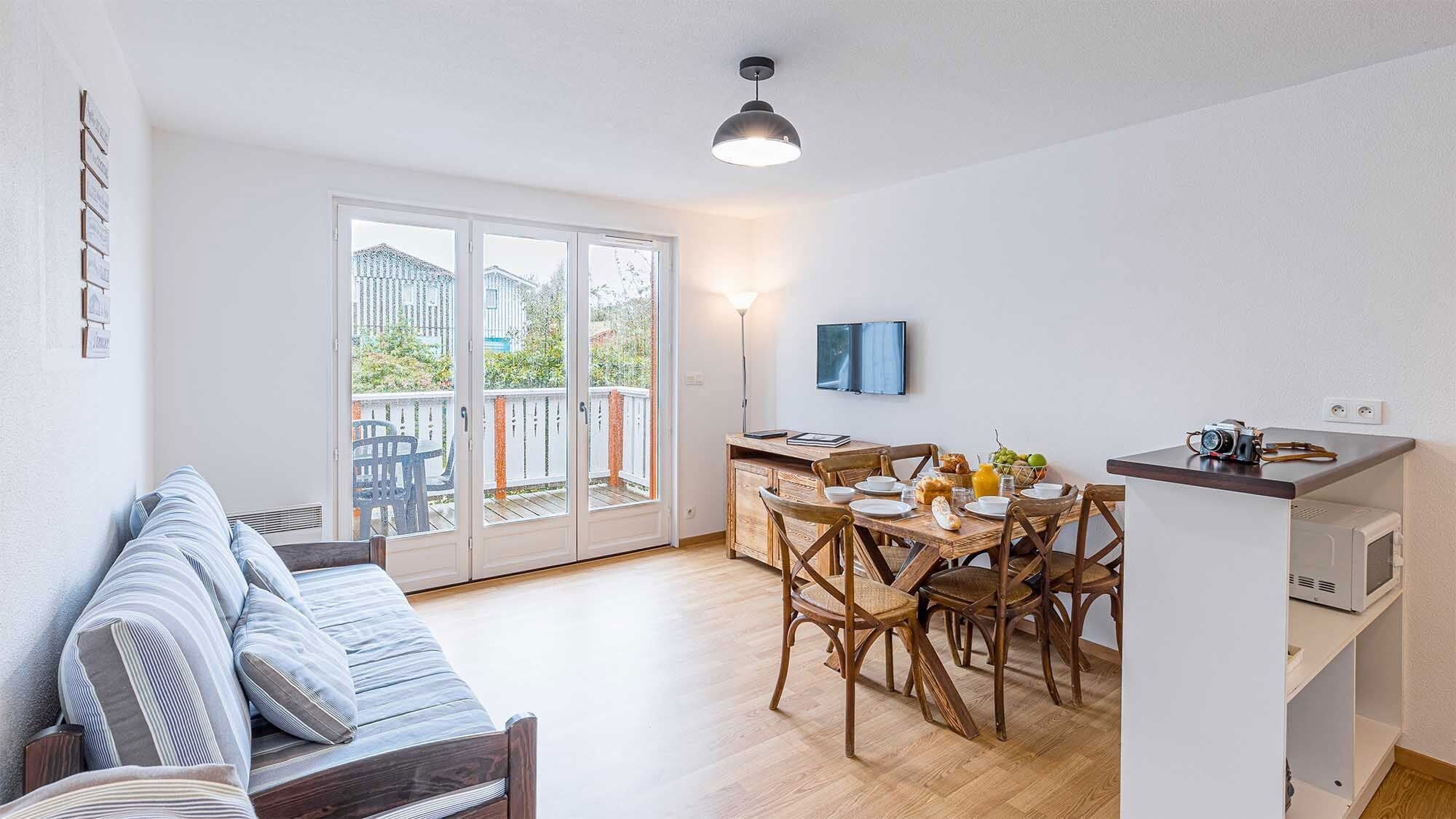 Un espace de vie compact comprenant un canapé, une table à manger, des chaises et un coin cuisine avec un téléviseur et des appareils électroménagers.