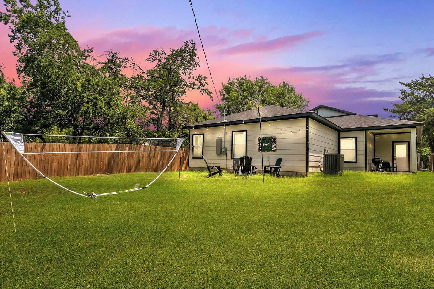 Une maison de plain-pied avec un jardin clôturé, un trampoline et un espace patio aménagé avec du mobilier d’extérieur.
