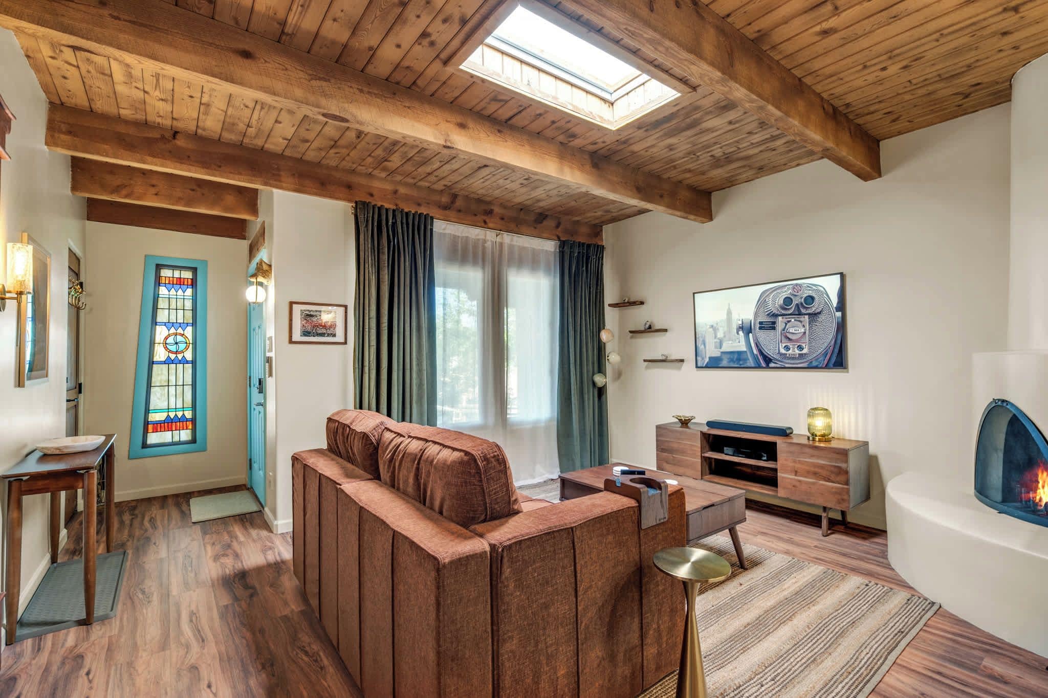 Ein gemütliches Wohnzimmer mit Holzbalkendecke, einem großen Fenster, einem Kamin und einem Fernseher.