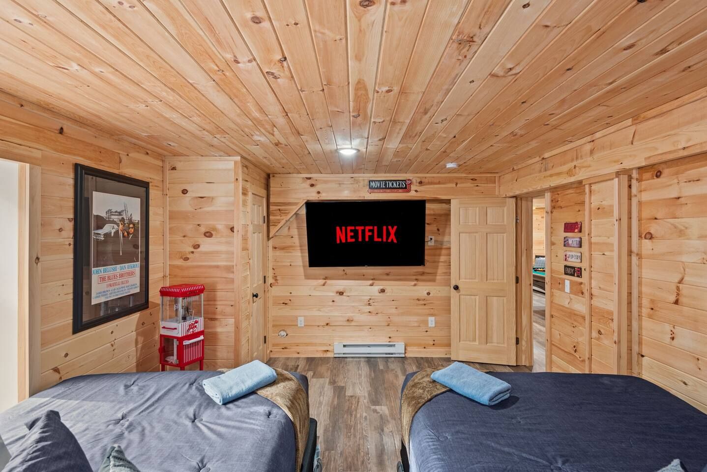 Une cabane en bois avec deux lits, un écran de télévision fixé au mur qui affiche « NETFLIX », et une affiche accrochée au mur.