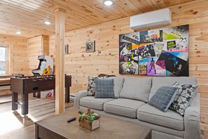 Ein gemütliches Zimmer mit Holzboden, einem grauen Sofa mit gemusterten Kissen, einem Kicker und einer Wand, die mit Vintage-Rockpostern dekoriert ist.