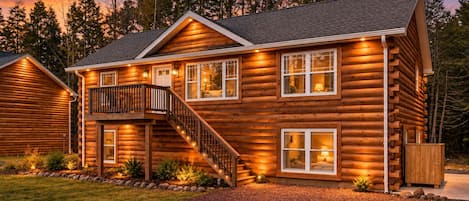 A log cabin with a balcony, multiple windows, and a staircase leading to the entrance.