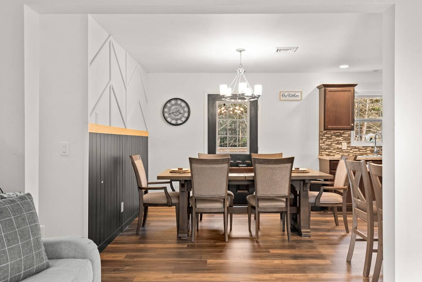 Un coin repas avec une table et des chaises en bois, un lustre et une horloge au mur.