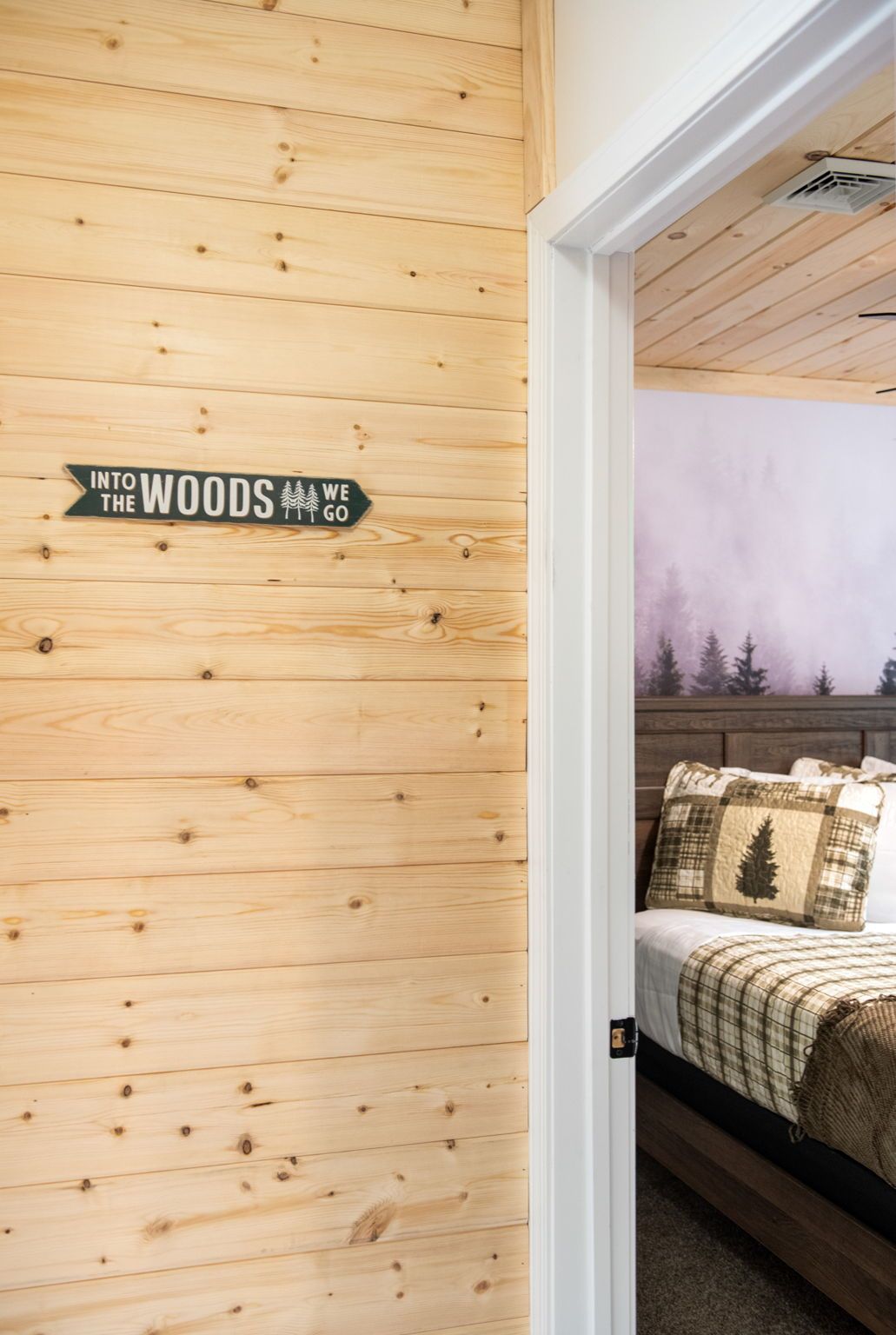 Una habitación con pared de madera y un letrero que dice 'INTO THE WOODS WE GO'.