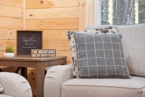 Ein gemütliches Zimmer mit einer Holzwand, einem gerahmten Motivationsspruch, einer kleinen Topfpflanze und einem karierten Kissen auf einem Sofa.