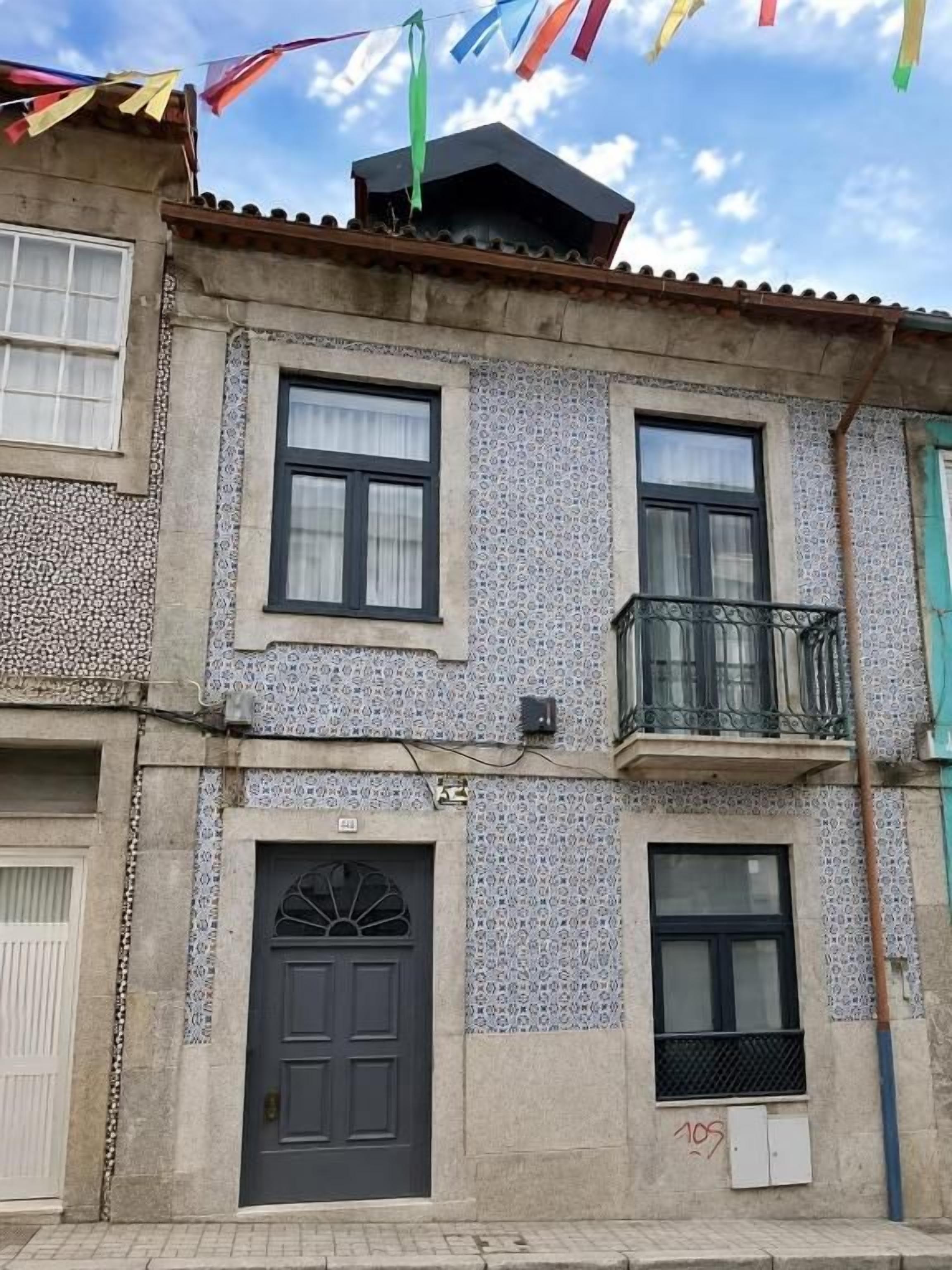 Un edificio con fachada de tejas, una puerta oscura y un balcón.