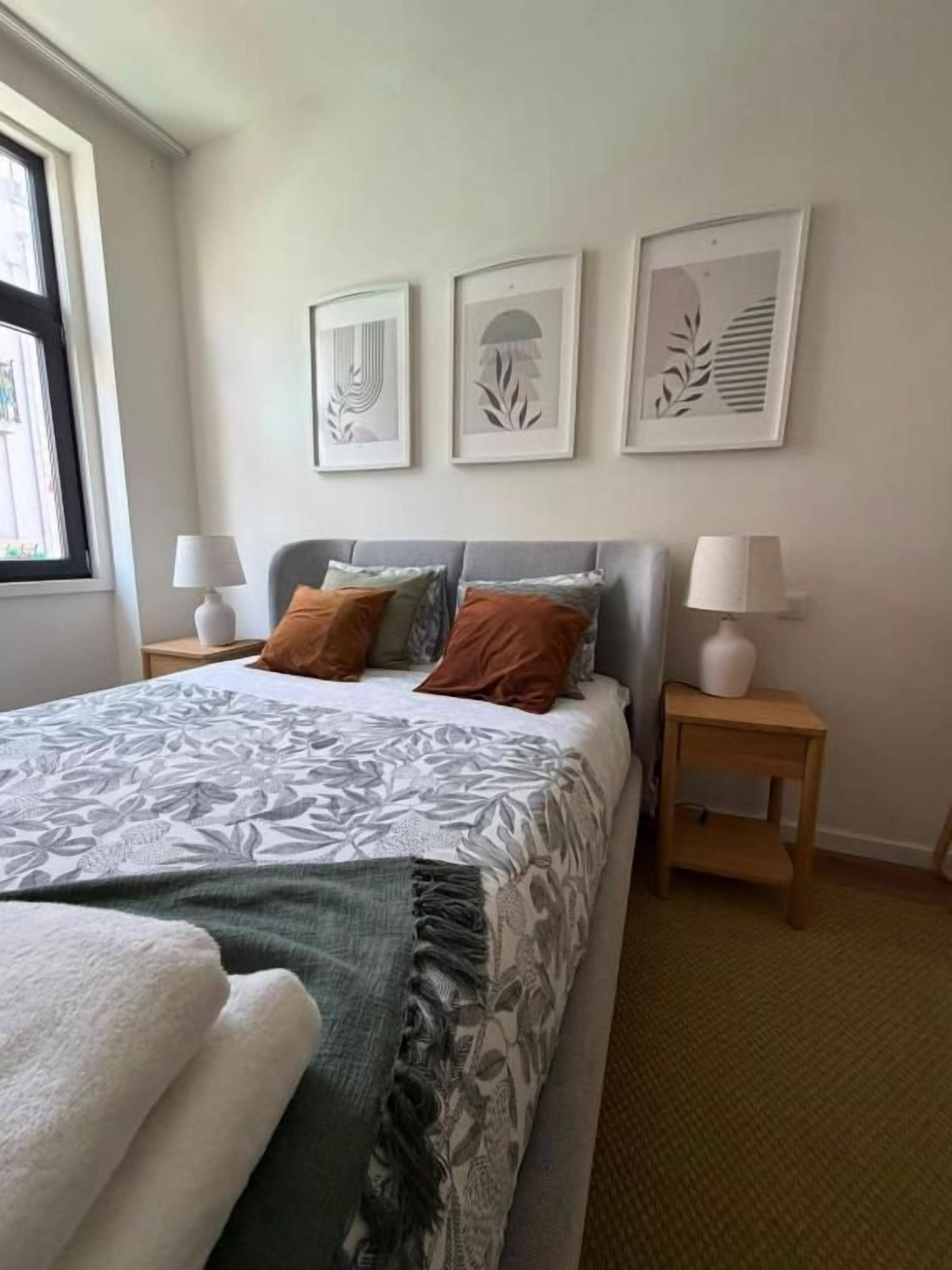 Un dormitorio con una cama, dos mesitas de noche y tres cuadros en la pared.