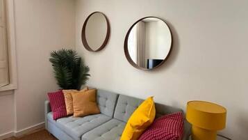 Een woonkamer met een grijze bank, twee ronde spiegels, een gele lamp en een klein tafeltje.