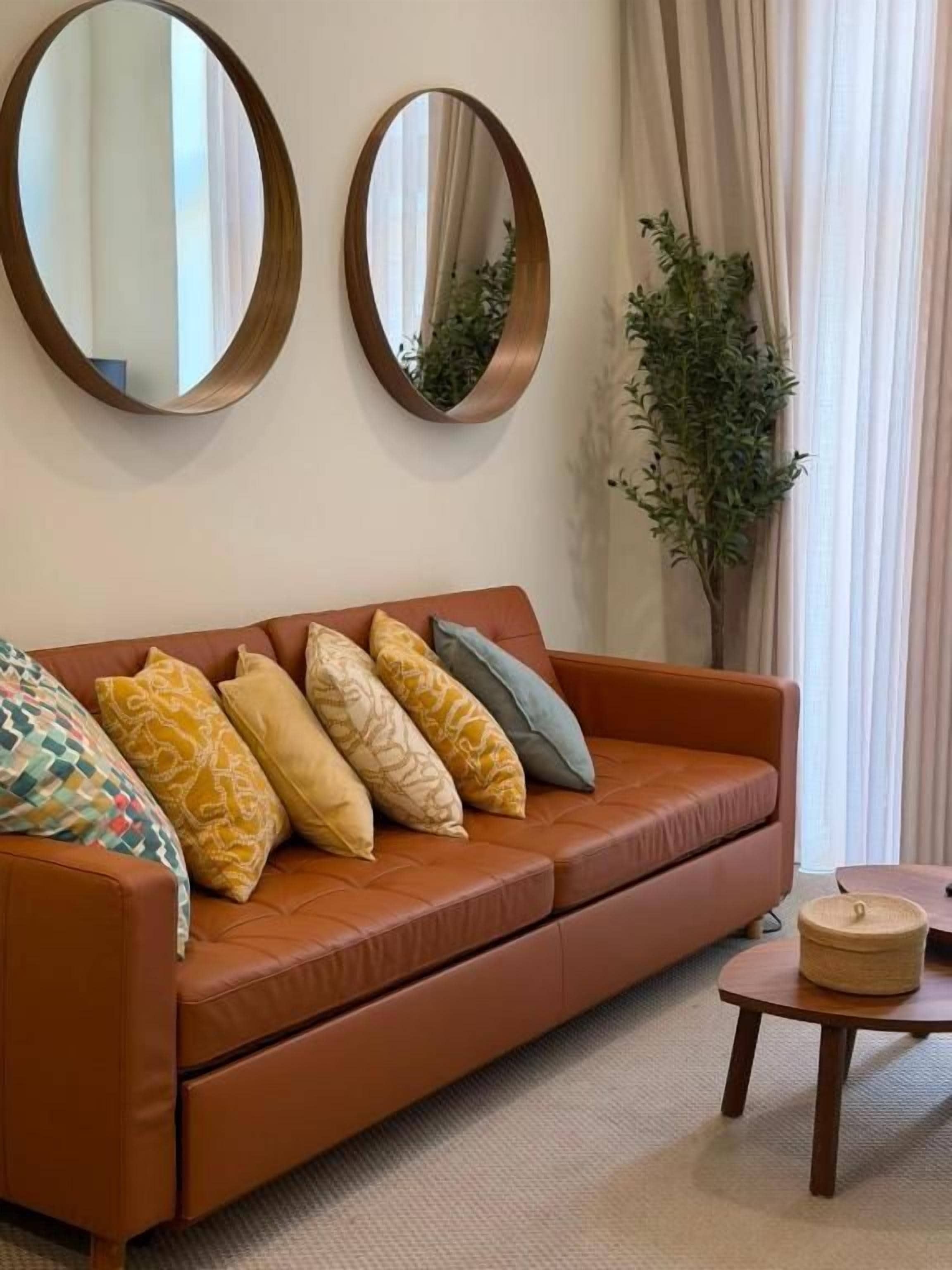 Un salon avec un canapé en cuir marron, deux miroirs ronds et une plante en pot.