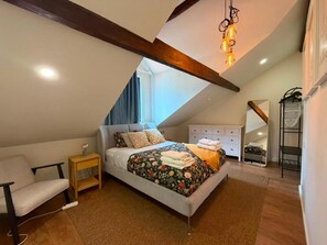 Un dormitorio con cama, mesitas de noche, una silla, cómoda y lámpara colgante.