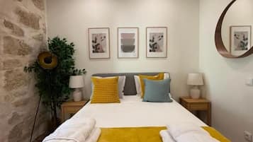 Ein Hotelzimmer mit einem Bett, einer gelben Tagesdecke und einem weißen Handtuch. An der Wand hängen gerahmte Bilder und es befindet sich ein runder Spiegel dort.