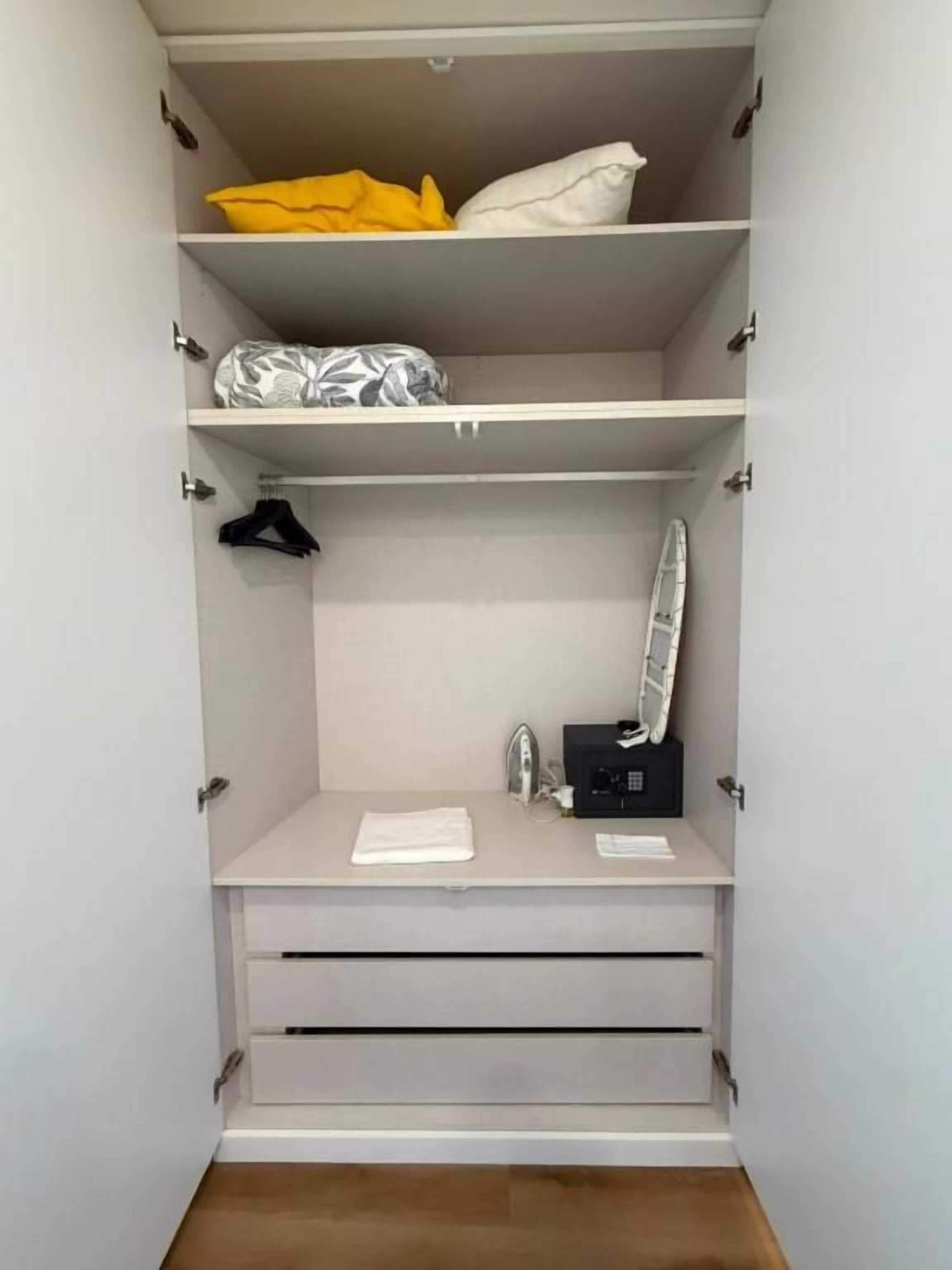A walk-in closet with multiple shelves, a hanging rack, and a small vanity area with a mirror and a black object.