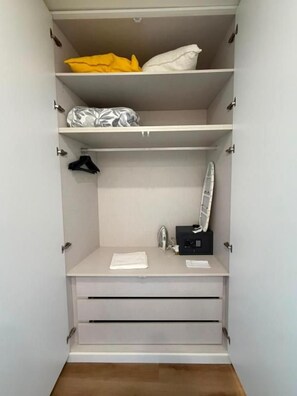 Un vestidor amplio con estantes múltiples, una barra para colgar ropa y una pequeña zona de tocador con un espejo y un objeto negro.