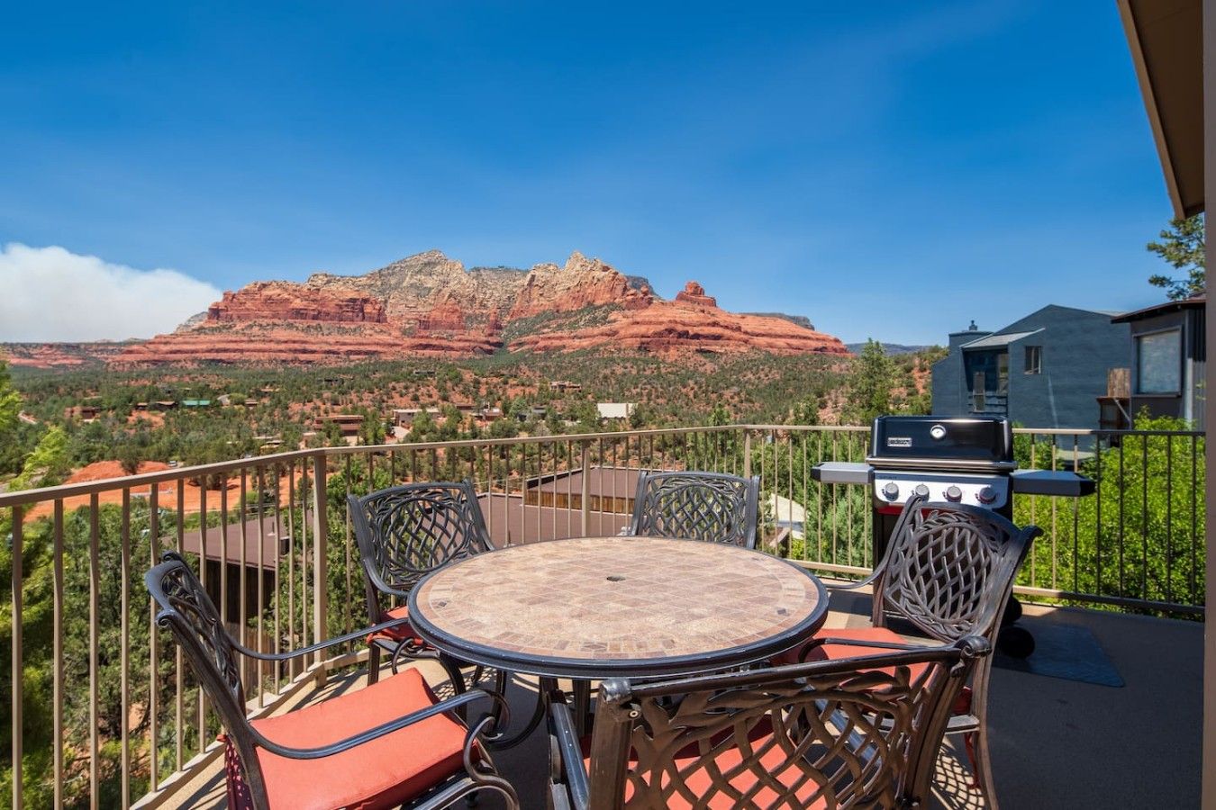 A balcony with a round table and chairs, a grill, and a view of red rock formations.
