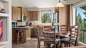 Een moderne keuken met houten kasten, een centraal eiland, barkrukken en een eettafel met stoelen.