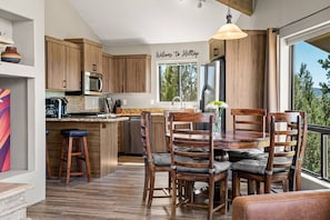 Een moderne keuken met houten kasten, een centraal eiland, barkrukken en een eettafel met stoelen.
