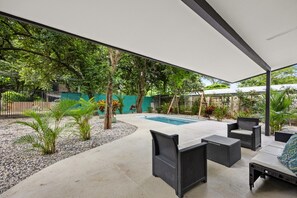 Ein überdachter Außenbereich mit Pool, Sitzgelegenheiten und viel Grün.