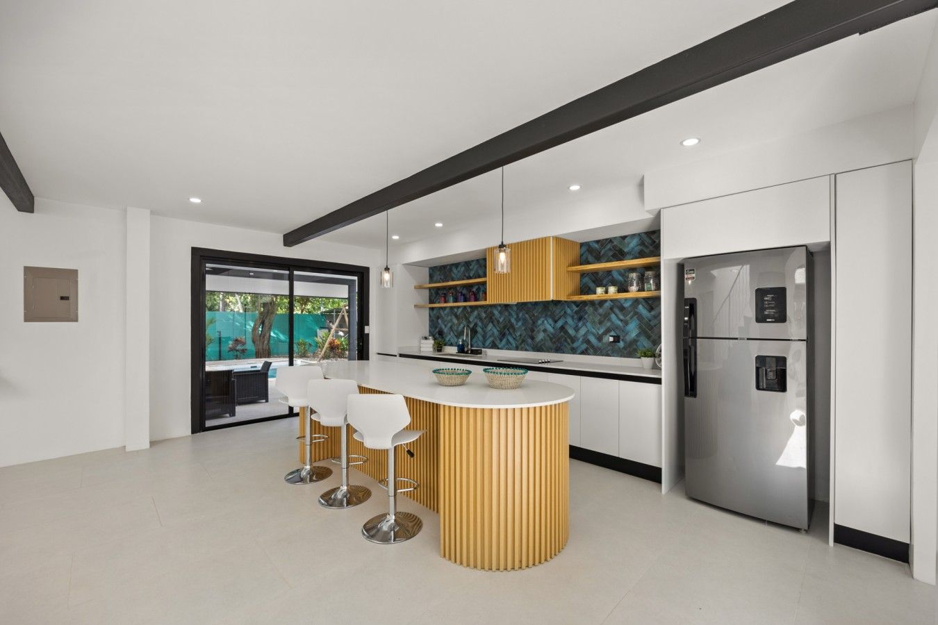 A modern kitchen with a central island, bar stools, a built-in refrigerator, and a herringbone backsplash.