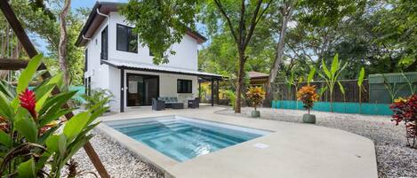 Una casa moderna con piscina, zona de estar exterior y abundante vegetación.