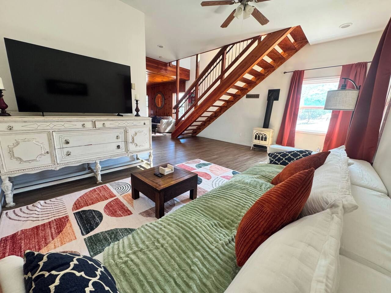 A living room with a television, a staircase, a sofa, and a patterned rug.
