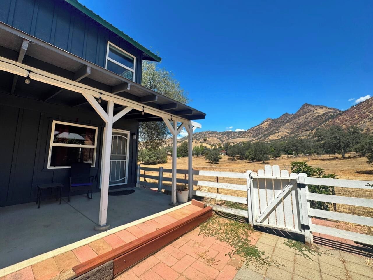A two-story building with a covered porch, a white fence, and a view of mountains.