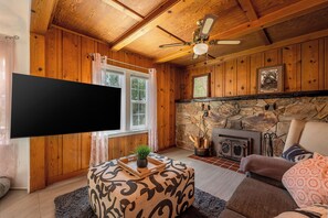 A cozy living room with wooden walls, a stone fireplace, a flat-screen TV, and a comfortable seating area. - Agate Ranch - Views | River Access | EV Charging (Three Rivers)