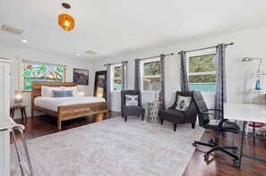 Ein Schlafzimmer mit einem Holzbett, zwei Sesseln, einem Schreibtisch und einem großen Fenster mit Vorhängen.