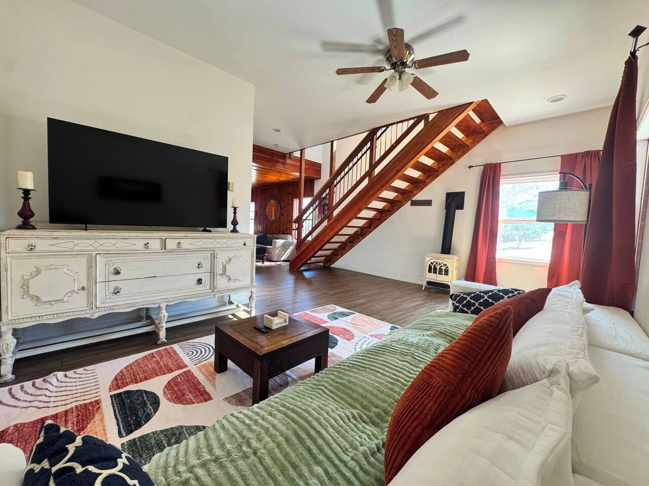Ein Wohnzimmer mit Fernseher, einer Treppe und einem großen Fenster.