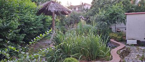 A garden with a variety of plants, a thatched structure, and a stone pathway.
