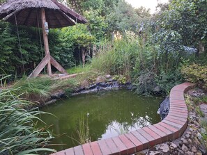 A pond with a brick walkway, surrounded by lush greenery and a thatched structure. - Spacious Home with fireplace, garden and ponds. (Kołobrzeg)