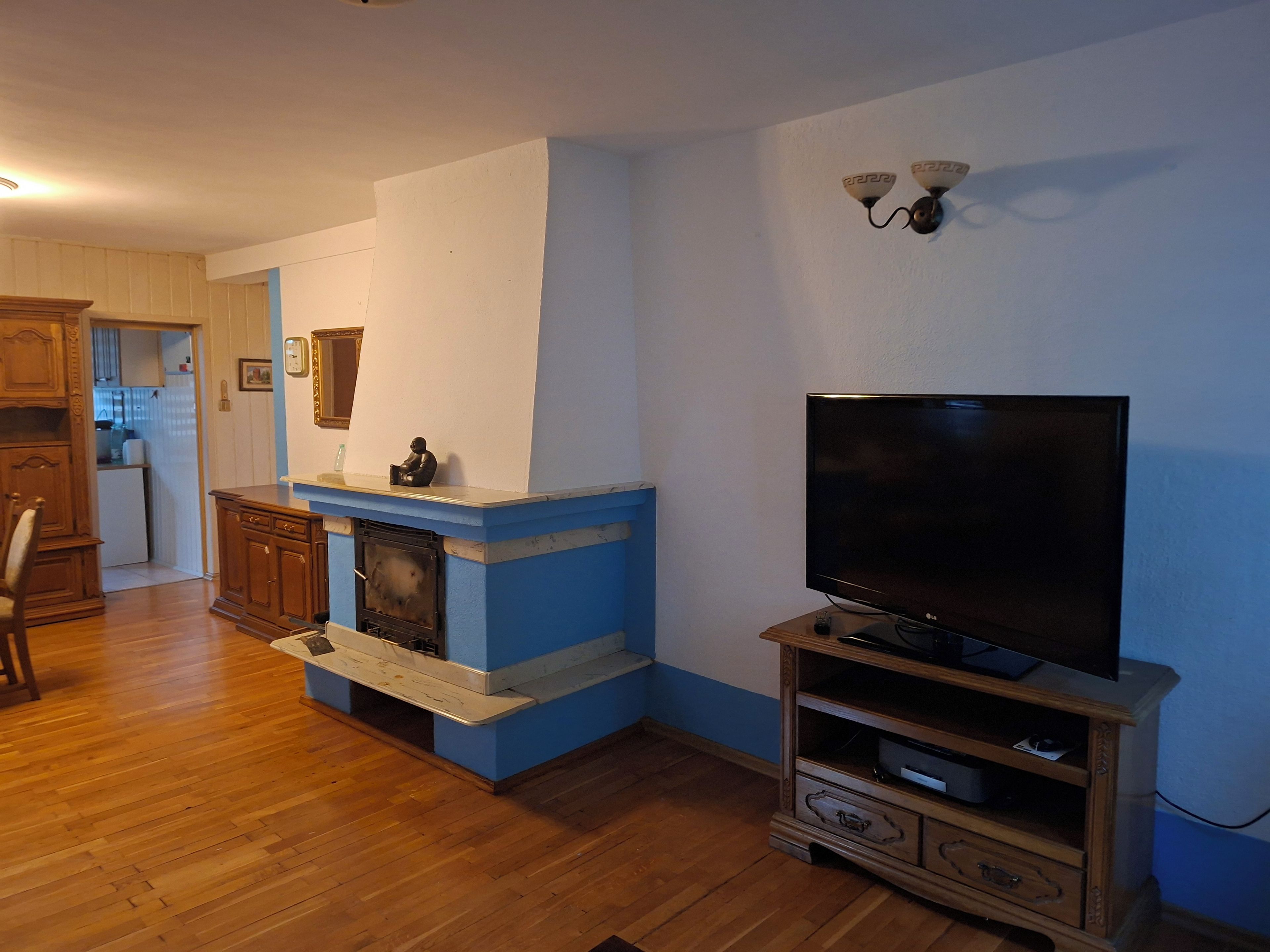 A living room with a fireplace, wooden cabinets, a television on a stand, and a kitchen in the background.